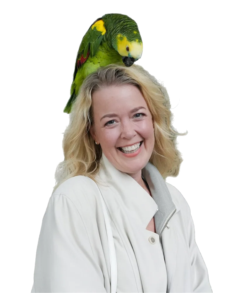 Aja Humm laughing with a green parrot perched on her head